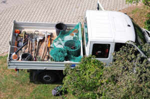 A landscaping truck pulled off the side of the road, the back of the truck holding many tools messily thrown in and without organization